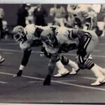 Black and white photograph of vintage football players in defensive stance during game action