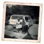 Three people standing in front of a station wagon with evergreen trees in background, vintage black and white photograph